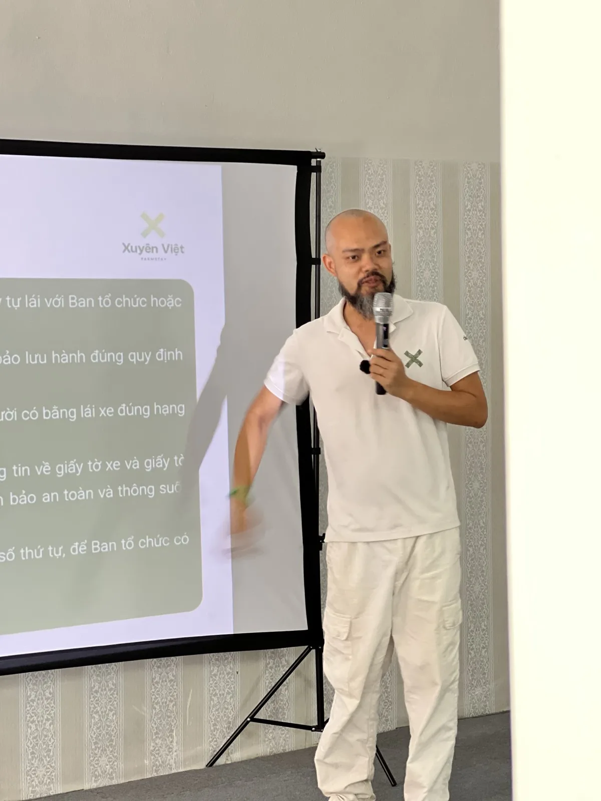 Phạm Thanh Tùng bước ra cạnh màn chiếu, tay dang sang bên khi giải thích quy định tự lái của đoàn Xuyên Việt