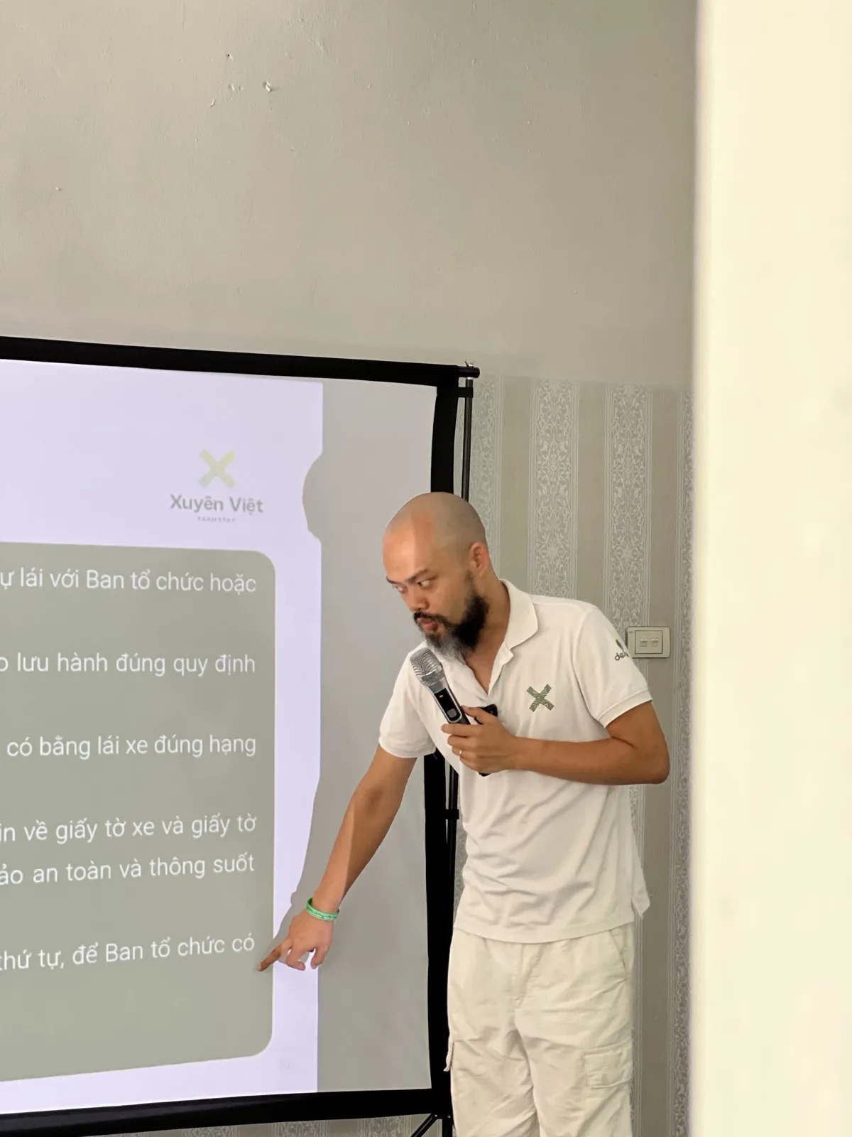 Phạm Thanh Tùng cúi người chỉ vào dòng cuối slide quy định đoàn xe Xuyên Việt, tay kia cầm micro