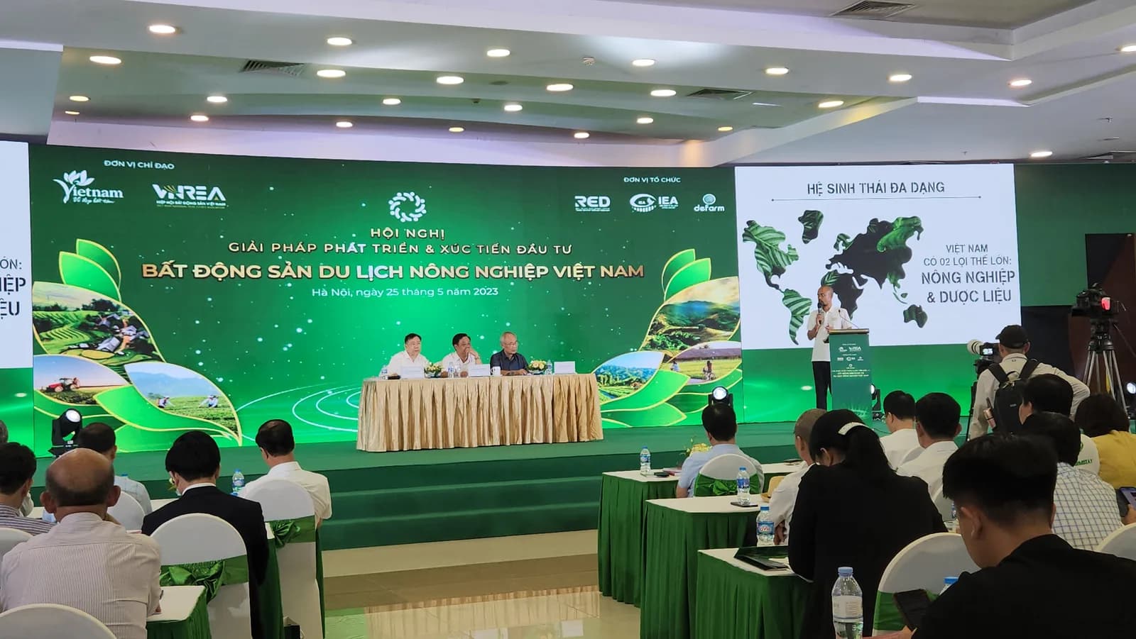 Phạm Thanh Tùng phát biểu tại Hội nghị Bất động sản Du lịch Nông nghiệp Việt Nam bên cạnh slide Hệ sinh thái đa dạng, phía dưới là đại biểu và phóng viên tác nghiệp
