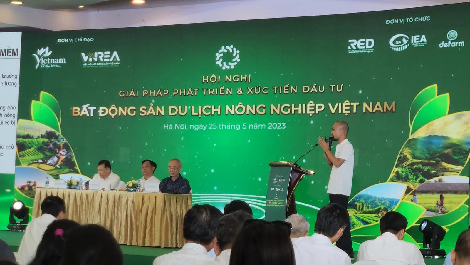 Toàn cảnh sân khấu Hội nghị Giải pháp Phát triển và Xúc tiến Đầu tư Bất động sản Du lịch Nông nghiệp Việt Nam, Hà Nội ngày 25/05/2023 — Phạm Thanh Tùng phát biểu trên bục, chủ toạ đoàn ngồi bàn bên trái